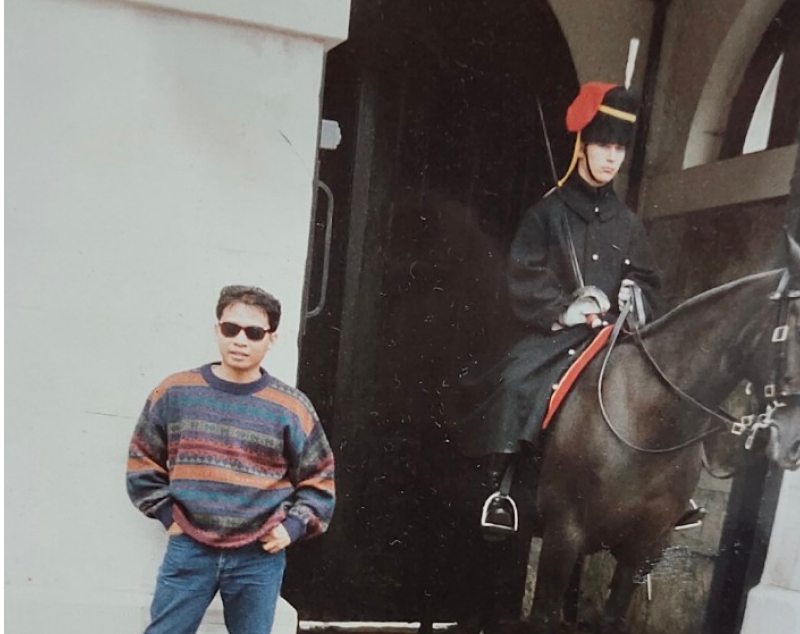 Acep stands beside a statue of a horse and guard in London